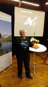 Deirdre Kelleghan holding her model of Cassini . In the background is her model of the planet Saturn . The venue is Castletown House and Parklands in Ireland . The event was Spectacular Cassini at Saturn a new drawing workshop by Deirdre 