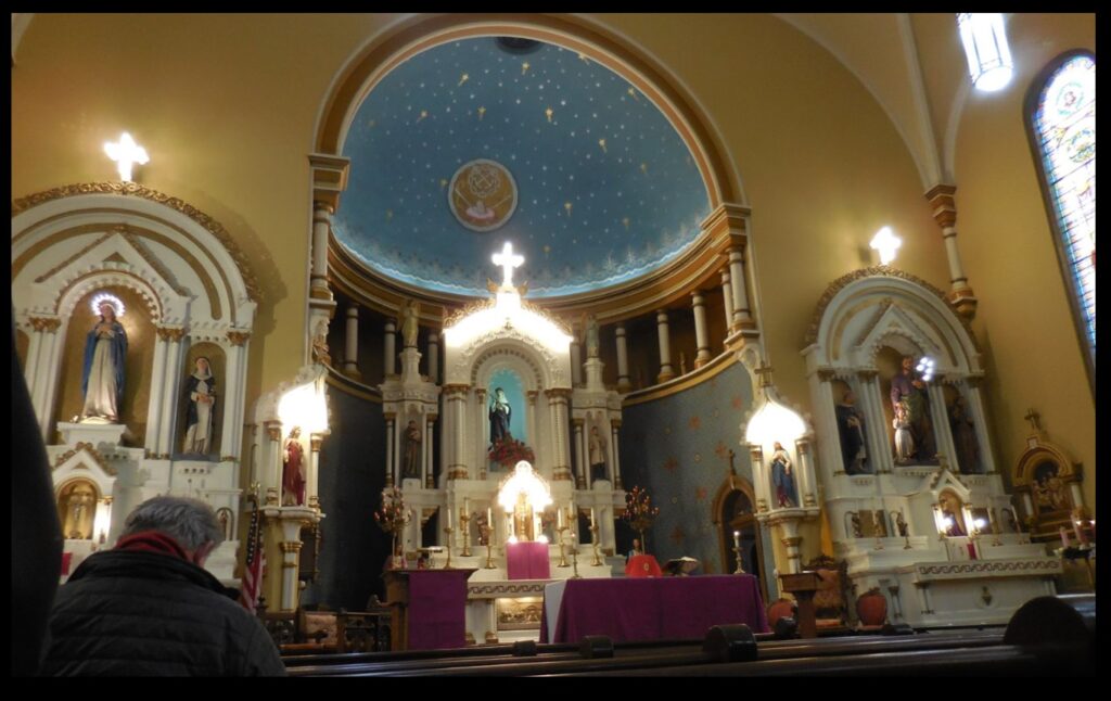 The front of St. Rose as seen from the pews.  This photo was taken on a cloudy day before noon mass in relatively low light, and the various alcoves in the church are illuminated, so the illumination really stands out.